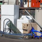 Refrigerator, dryer, filing cabinet, bumper, fence, bike frame and water heater propped up for display and recycle