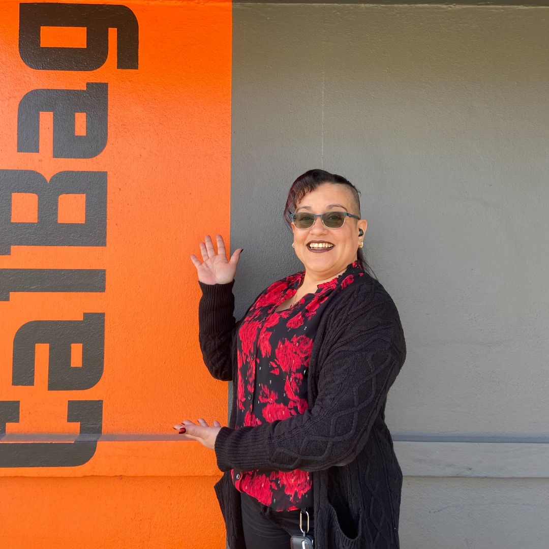 Kisha standing in front of Calbag metals, pointing to the Calbag name painted on the building